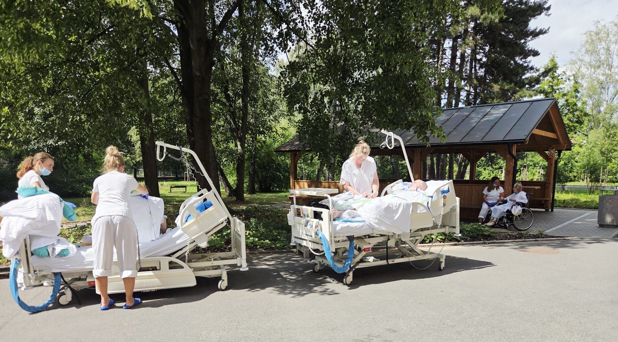 Pacienti na lůžkách se zdravotnickým personálem venku mezi stromy.