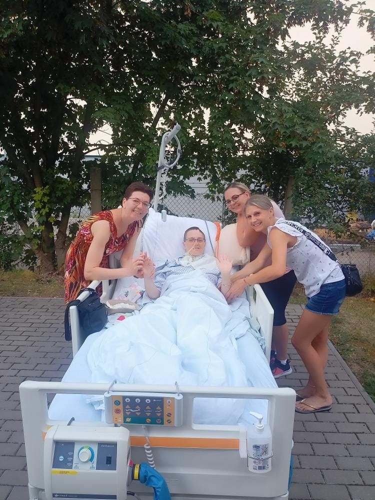 Dvě ženy u pacientky na lůžku na zahradě