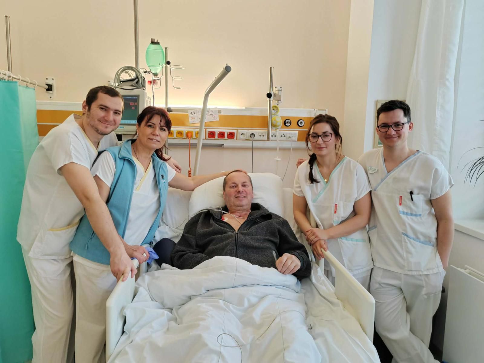 Pacient na lůžku a členové týmu v pokoji
