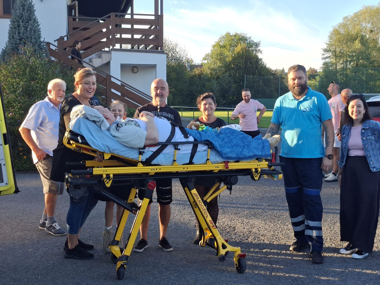 Pacient na přepravním lůžku se svými blízkými a doprovodem Sanitky přání.