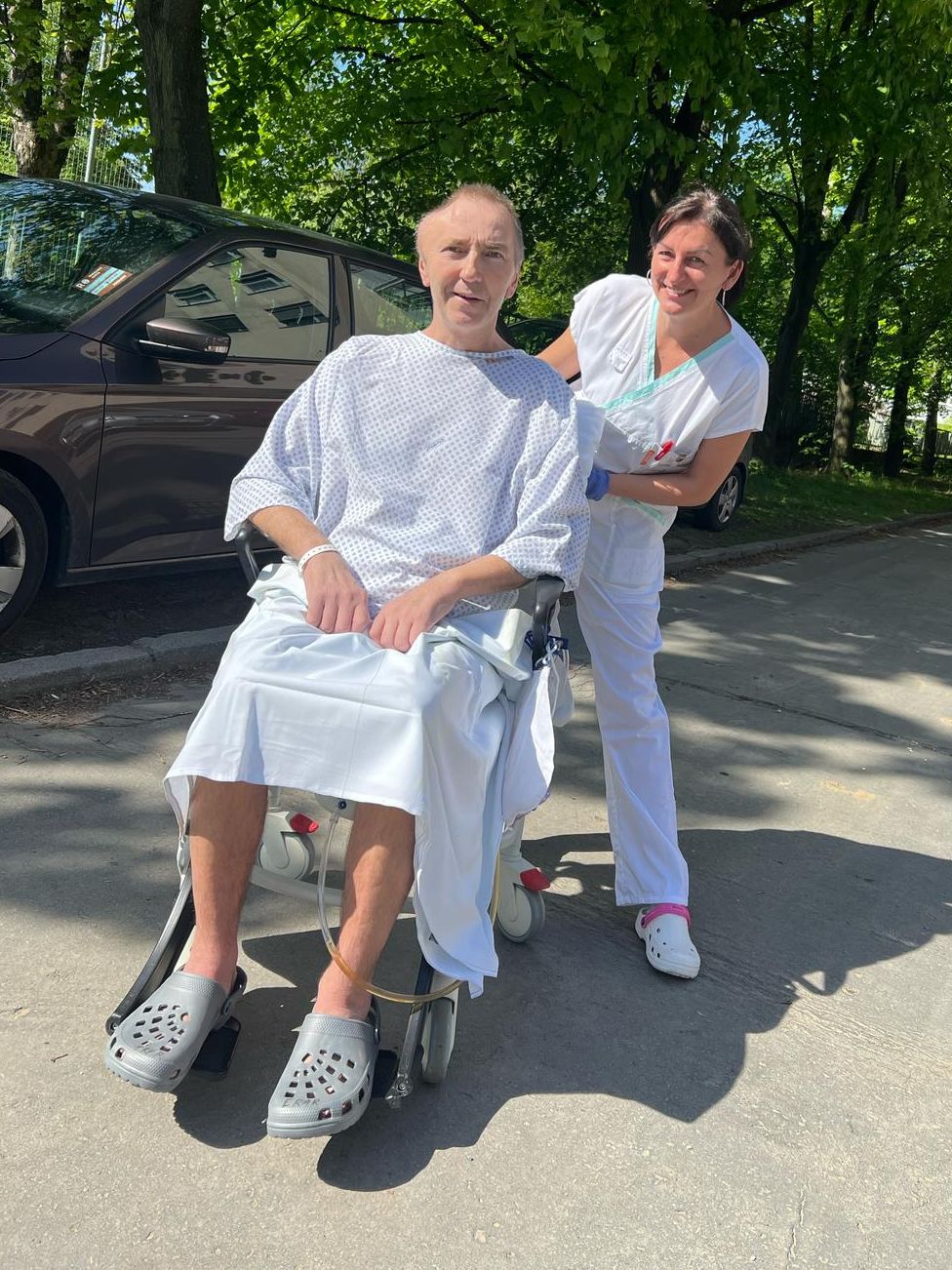 Pacient na vozíku se zdravotnicí před budovou.
